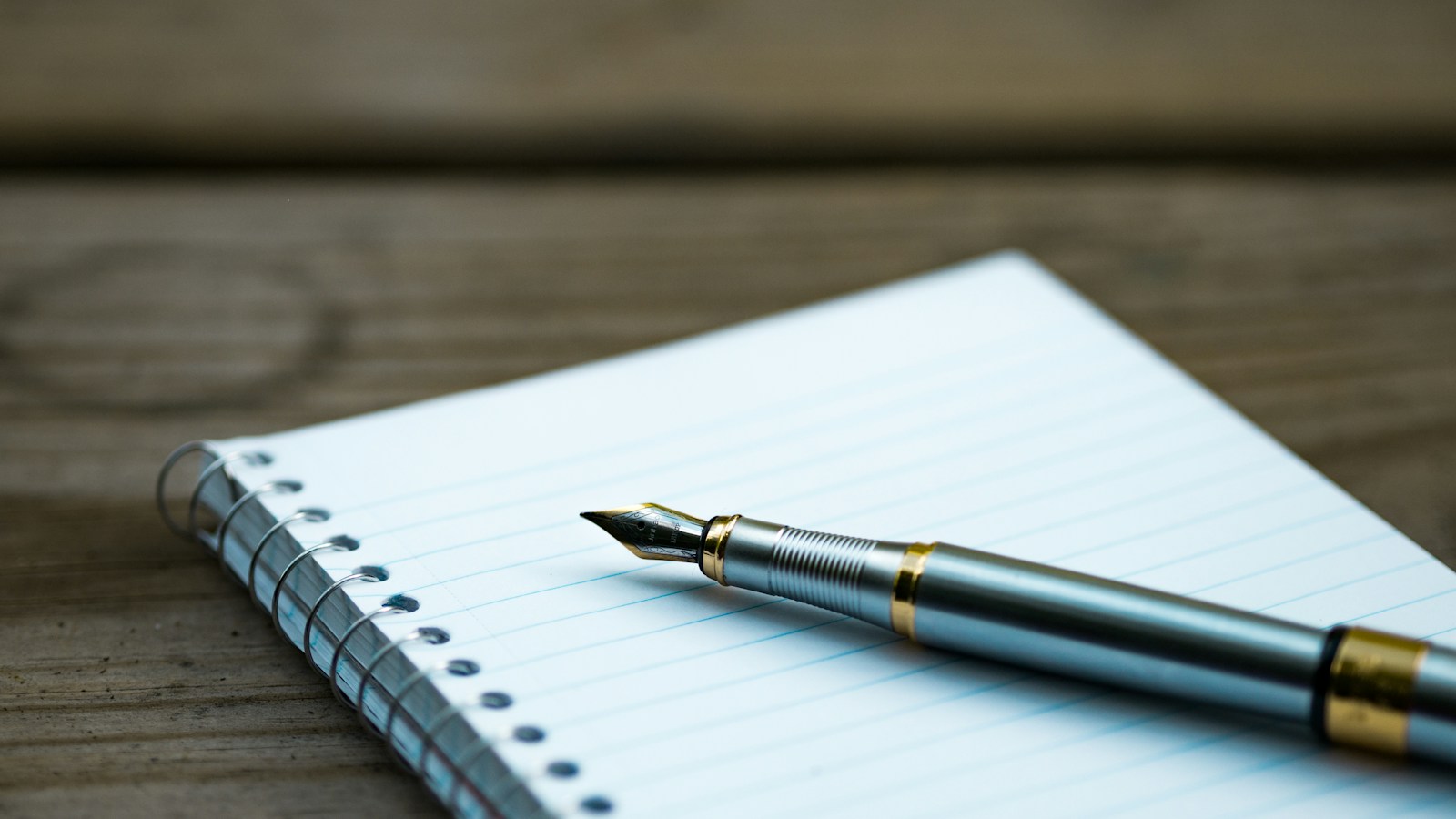 Fountain pen resting on a lined spiral notebook on a wooden desk