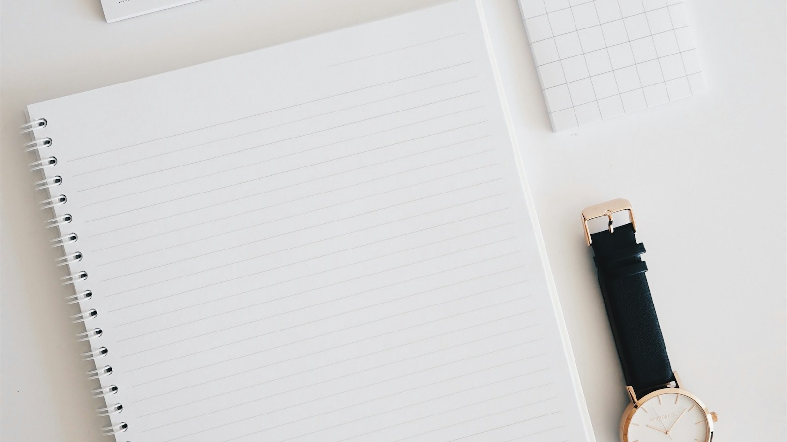 Open lined notebook and watch on a clean white desk